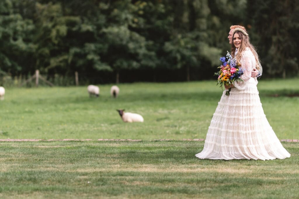 bride and groom walking at burtonfields hall york with sheep in the background