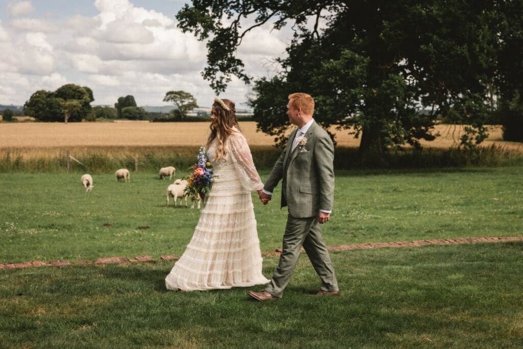 Bride and groom walking on the fields at burton fields hall in york with sheep in the background