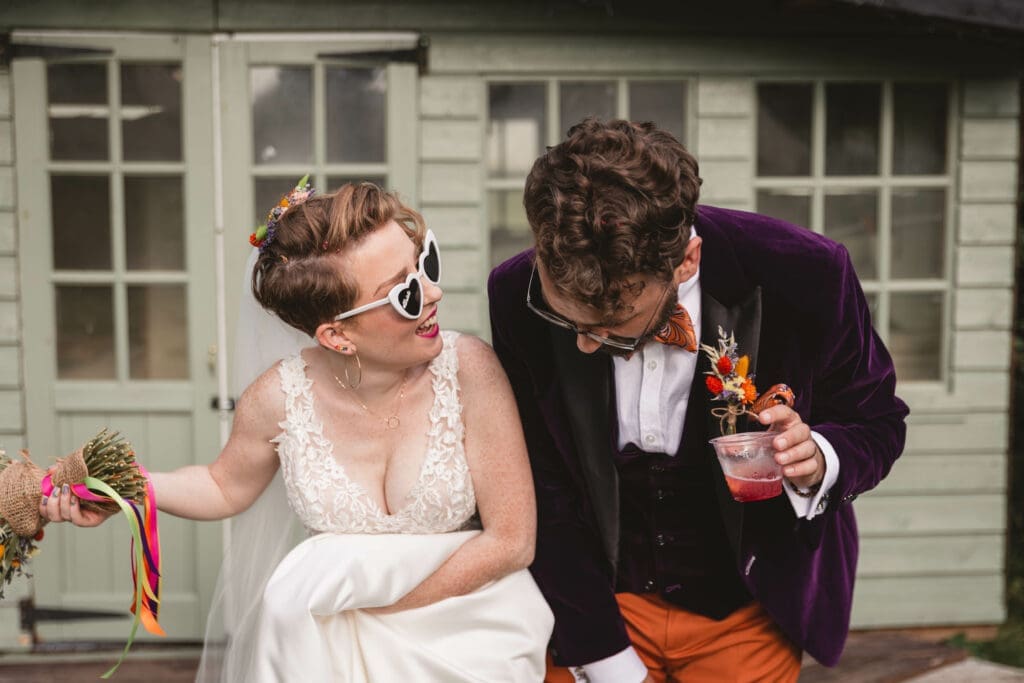 A Bride with heart shapped sunglasses laughing with the groom dressed in a purple velvet suit | Yorkshire wedding photographer