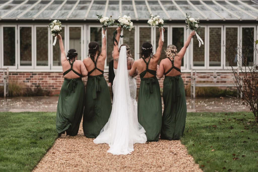 Bridesmaids dressed in green holding flowers in the air walking away at | WEdding photographers near me