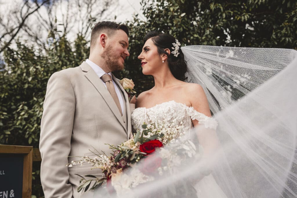 Bride with vail in the wind holding rose red flowers at sandburn hall hotel