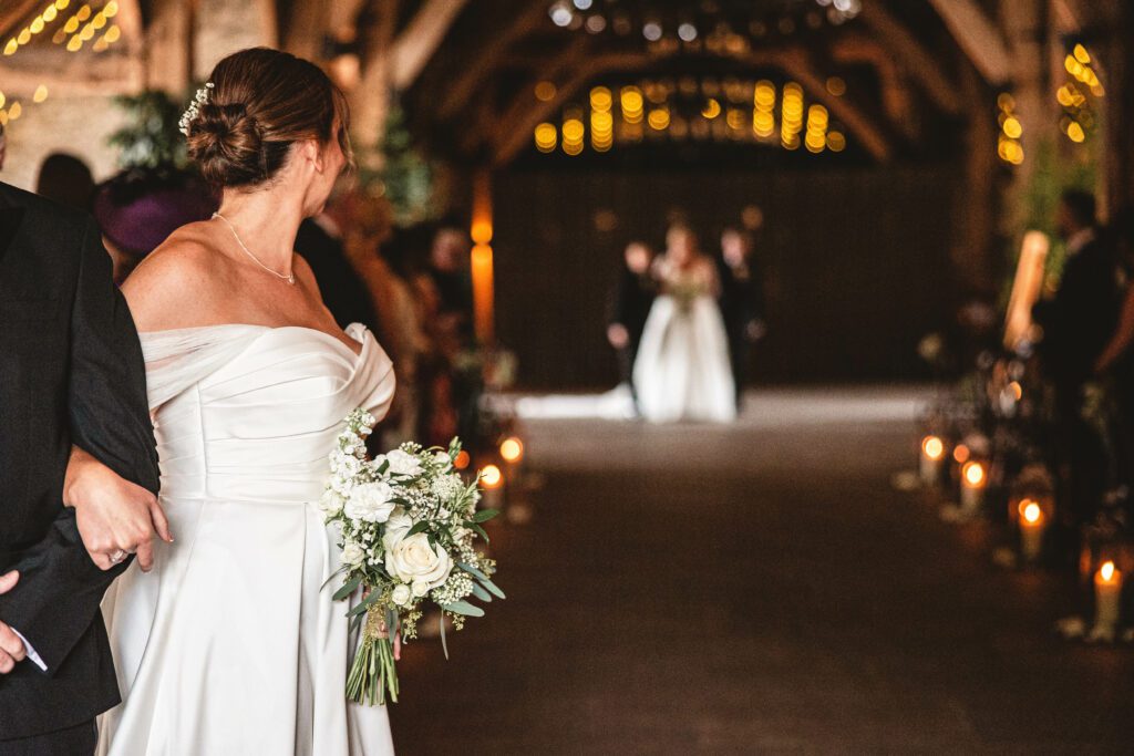 Bride turning around to see her bride walking down the aisle at the tithe barn whilst all the guests turn around to see her for the first time