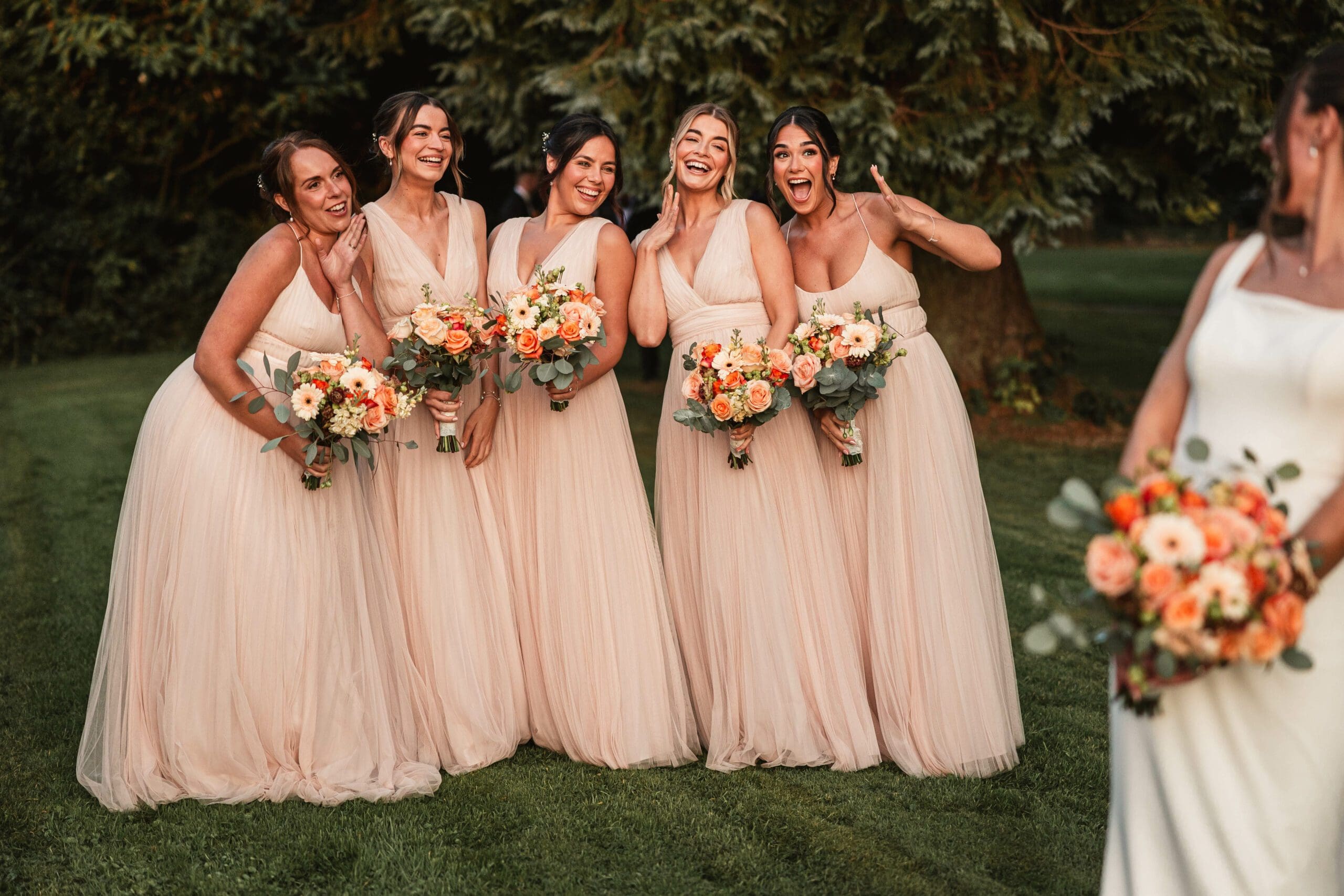 Bridesmaids with autumn flowers looking happy at the bride with golden sun in the gardens of the Tithe Barn | Tithe barn wedding photographer