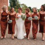 Bridesmaids in bronze outifts walking along side bride holding there flowers for some fun wedding photos at hodstck priory for there wedding | Hodsock priory wedding photographer