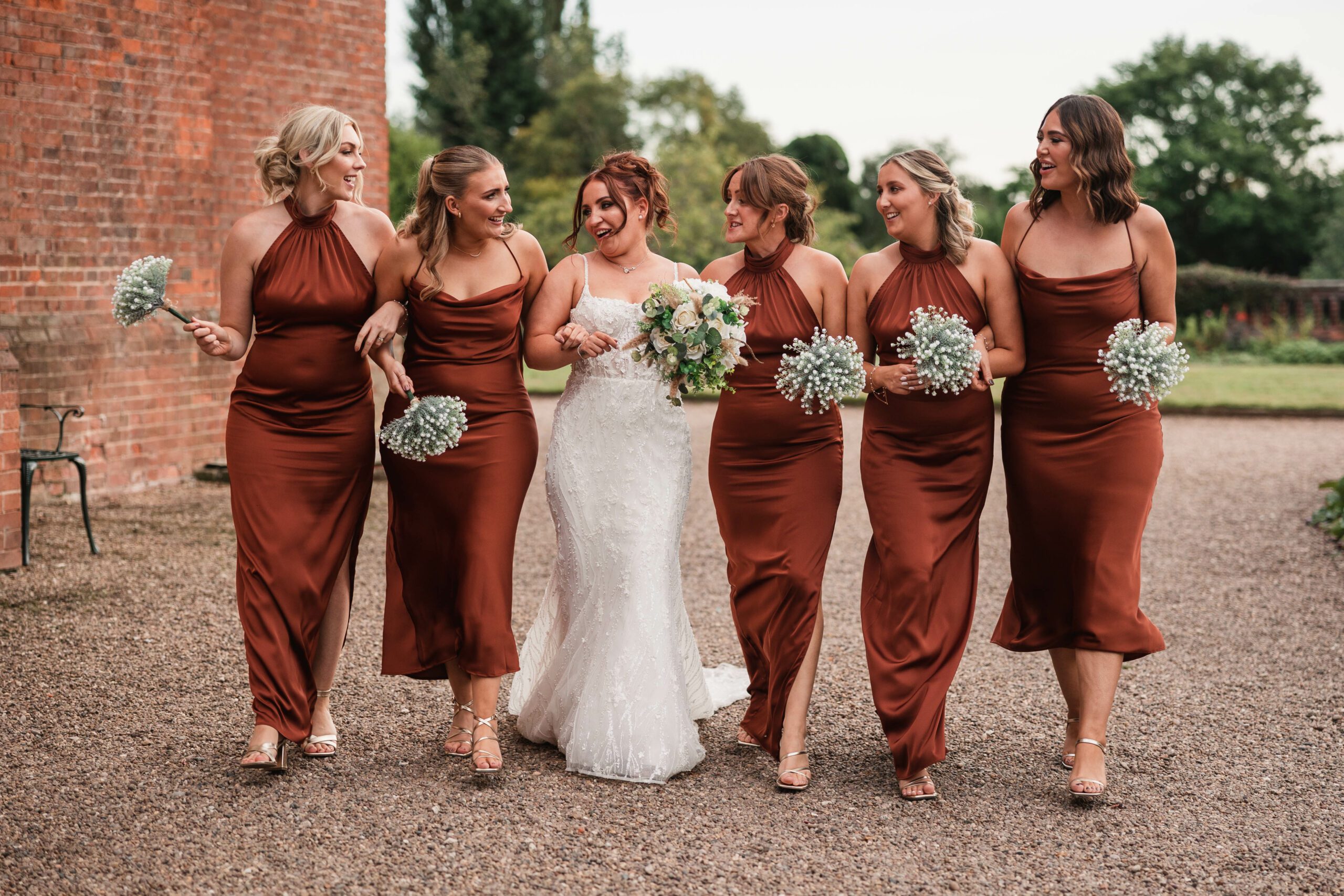 Bridesmaids in bronze outifts walking along side bride holding there flowers for some fun wedding photos at hodstck priory for there wedding | Hodsock priory wedding photographer