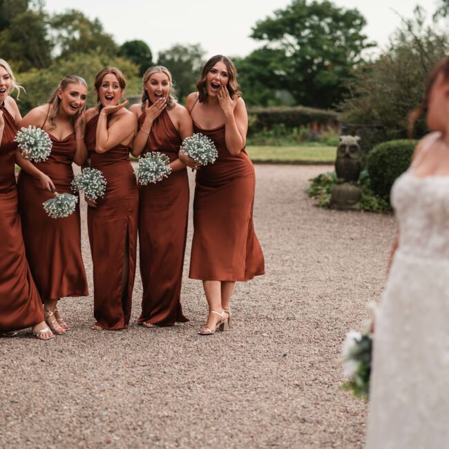 Bridesmiads dressed in bronze dresses looking in disbelieve at a beautiful bride at hodsock priory| Hodsock priory wedding photographer