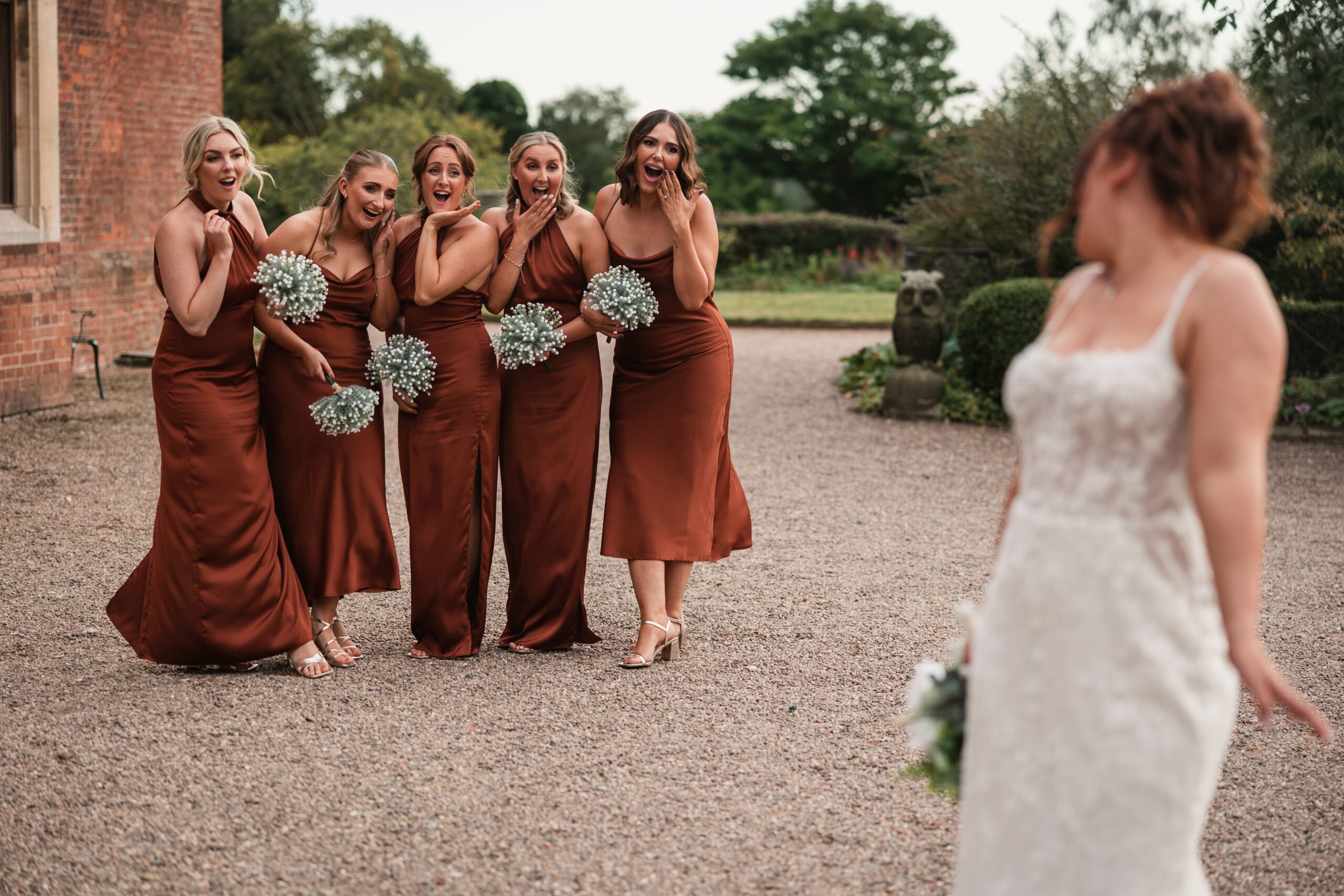 Bridesmiads dressed in bronze dresses looking in disbelieve at a beautiful bride at hodsock priory| Hodsock priory wedding photographer