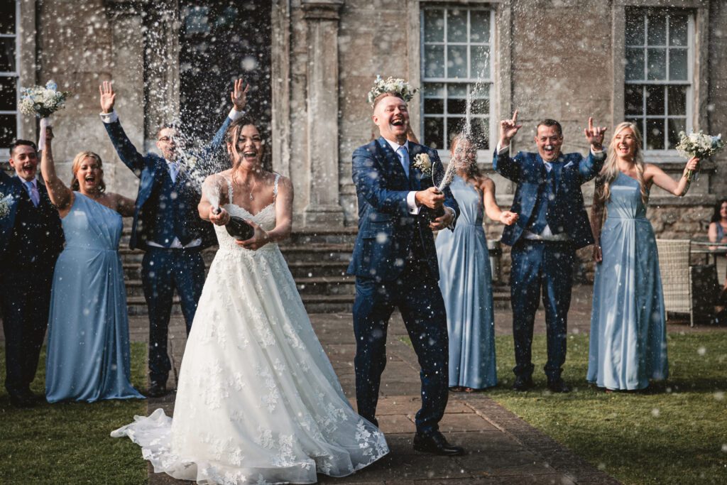 Bridesmaids in sky blue and groosmmen in navy blue outfits to a champagne spray photo | Yorkshire Wedding Photographer