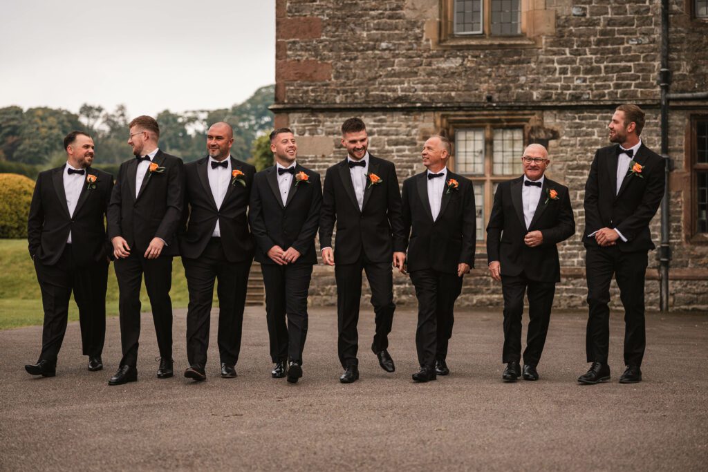 Groomsmen walking together dressed in black tuxedo outfits chatting at tissington hall | Tissington hall wedding photographer