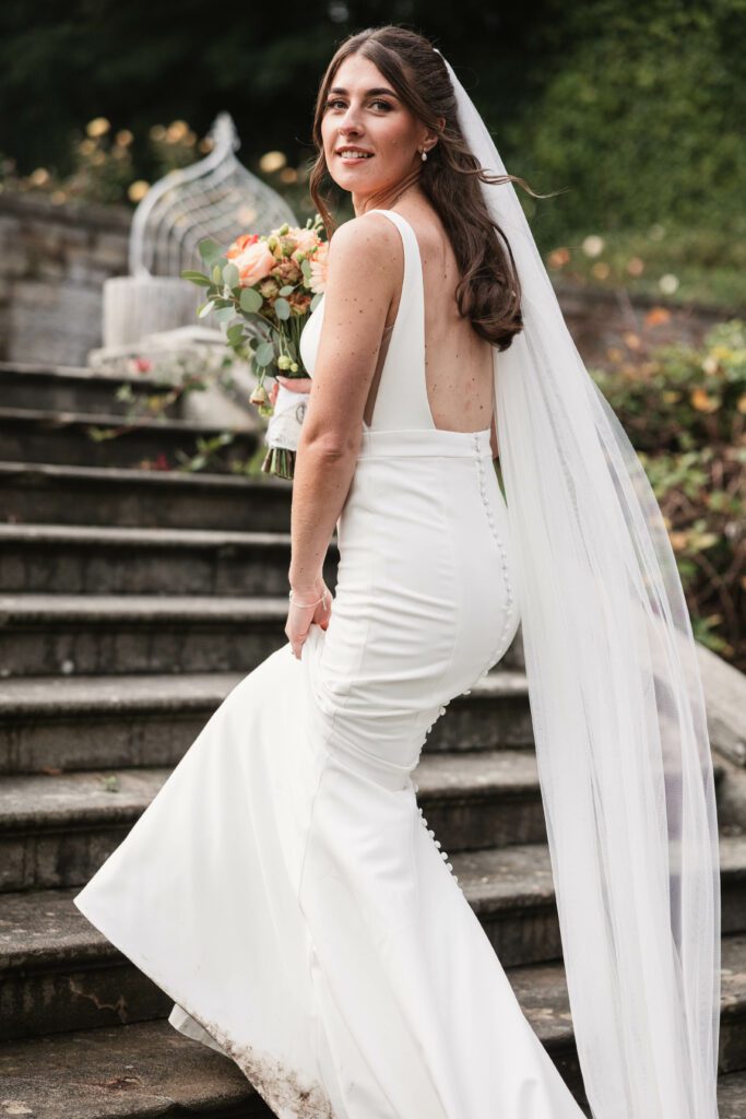 Bride walking up the stairs at tissington hall looking back dressed in a white dress | Wedding photographer tissington