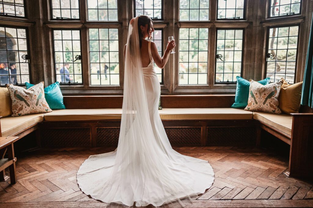 Bride in the window drinking prosecco at tissington hall | Tissington wedding photographer