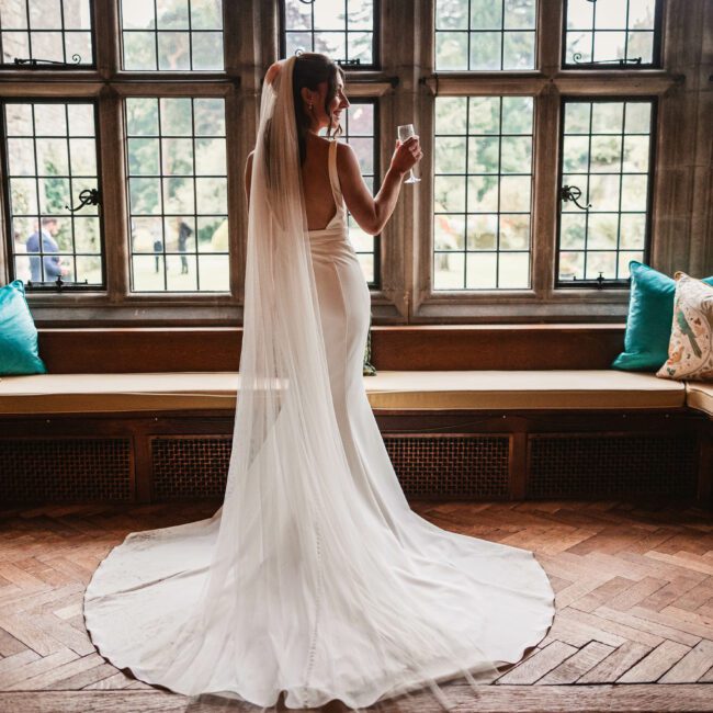 Bride in the window drinking prosecco at tissington hall | Tissington wedding photographer