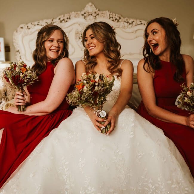 Bride and her bridesmaids laughing to each other - bridesmaids dressed in red outfits at mosbrough hall