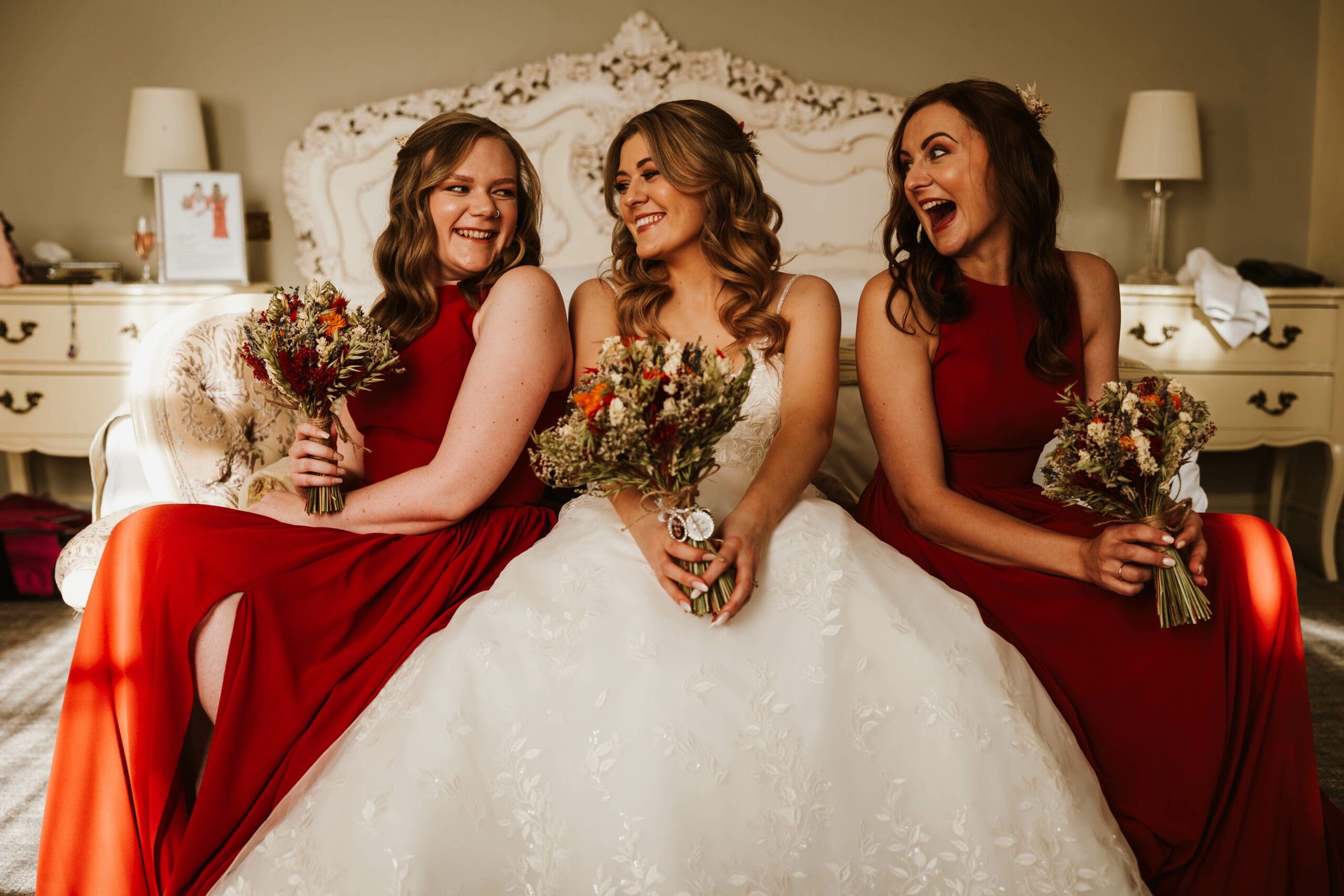 Bride and her bridesmaids laughing to each other - bridesmaids dressed in red outfits at mosbrough hall