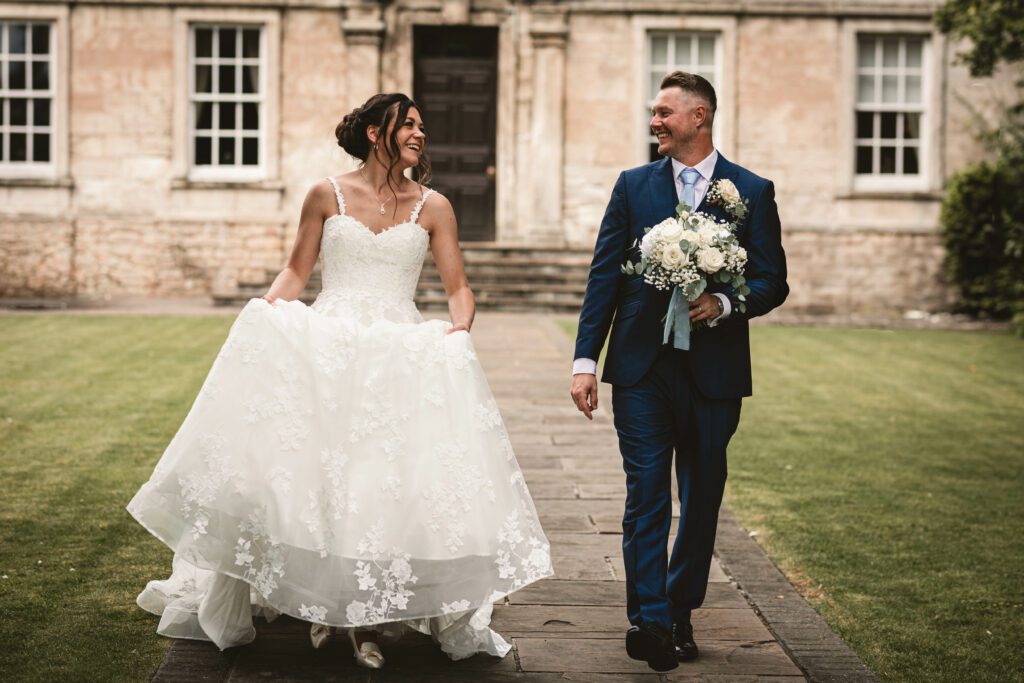 A bride and groom walking together as the groom holds the flowers and the bride holds her dress taken at Hellaby hall hotel | South yorkshire wedding photographer